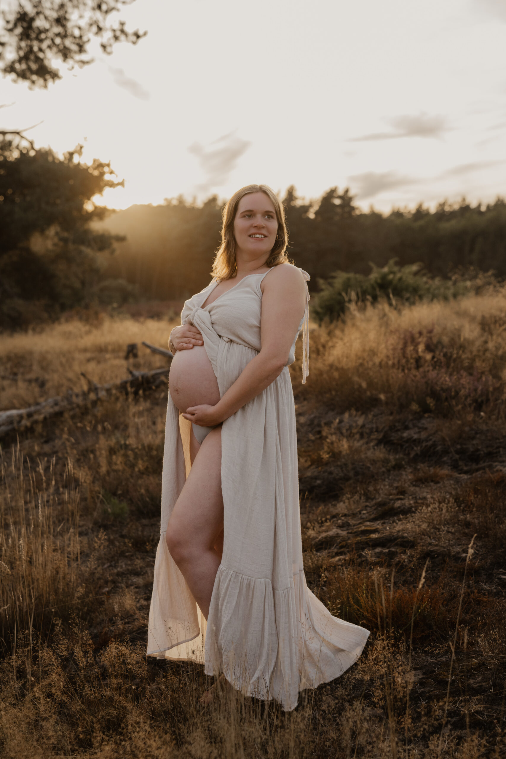 Zwangere vrouw in cremekleurige jurk in het avondlicht tijdens een zwangerschapsshoot in de Achterhoek