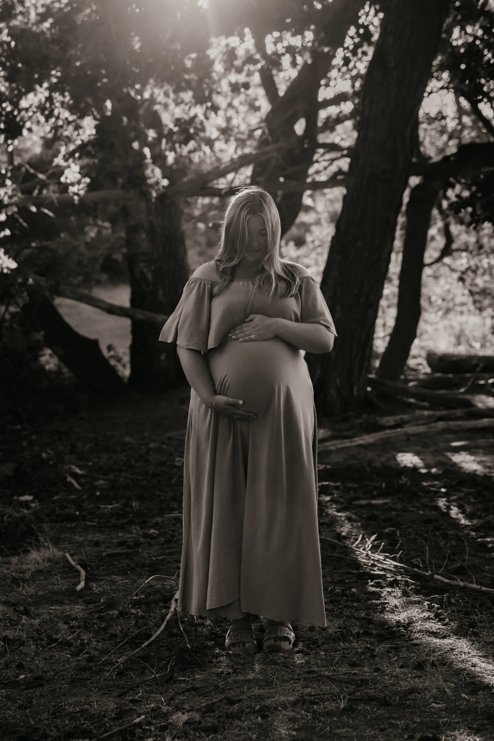 Zwart-witfoto van een zwangere vrouw met haar handen om haar buik in het bos